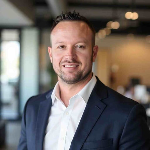 Professional headshot of Aaron Ammerman in a dark blazer and white shirt, standing in a modern office