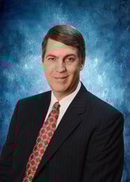 Professional headshot of Phil Willard wearing a dark blazer and patterned tie against a blue gradient background